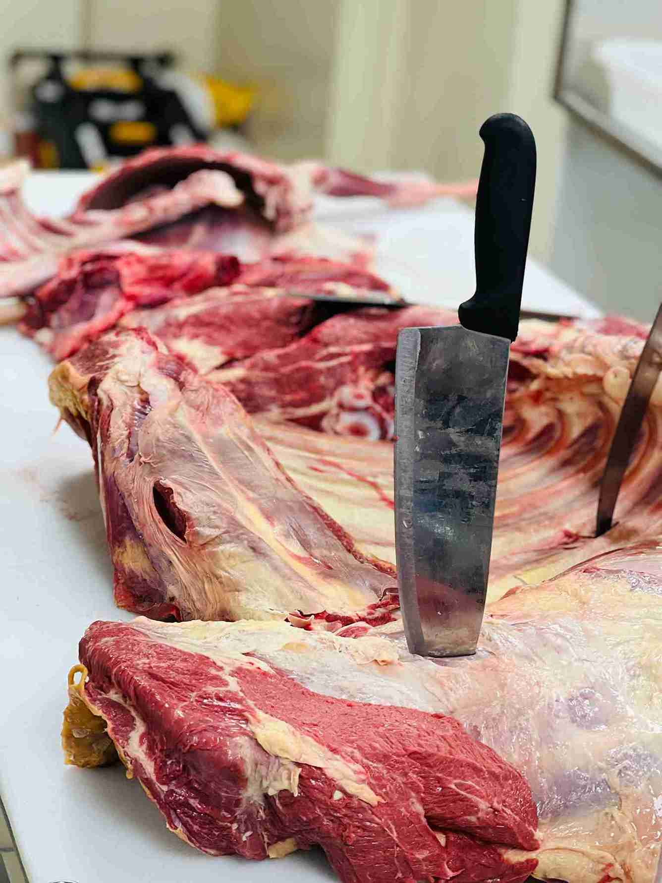 Butcher processing a large primal cut of beef on a block with a cleaver at Bismillah Grocery & Meat Market.