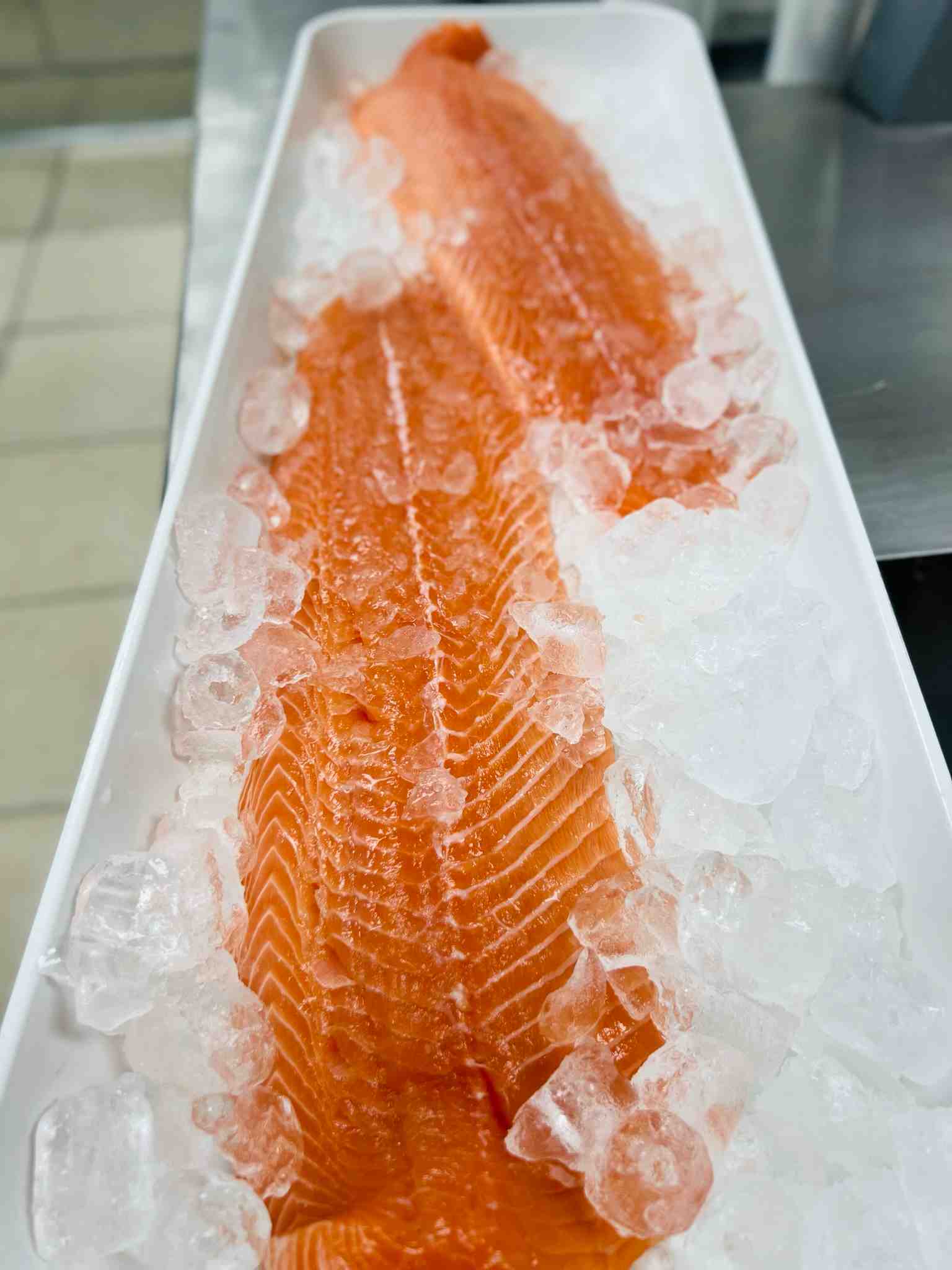 Fresh, skin-on Salmon Fillets displayed on a bed of crushed ice at Bismillah Grocery & Meat Market.